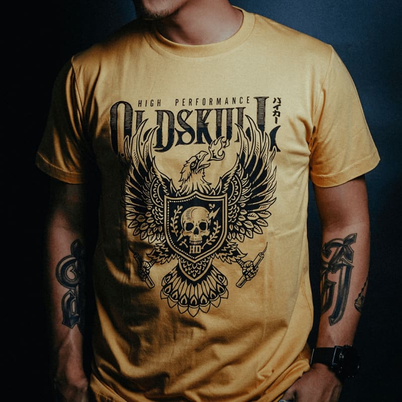 This shirt comes in yellow gold, black or white.  It has a eagle emblem with a shield in the center containing a skull with lightning through it.  The brand name Oldskull Shirts is written above it in bold print.  This is a streetwear vintage style of shirt made of the coolest design  by Oldskull Store USA the best in North America.