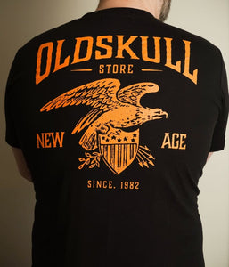 This shirt is similar to the Harley Davidson style of shirts.  It is black with orange print.  It has a small Oldskull Shirts logo on the front.  On the back it has an large eagle over a shield design with the words Oldskull Store written over it.  It is a vintage streetwear design. 